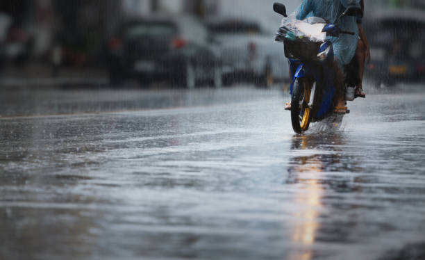 A couple with raincoat on a motorbike during hard rainfall/Dramatic scene of rainy season in Southeast Asia). stock photo