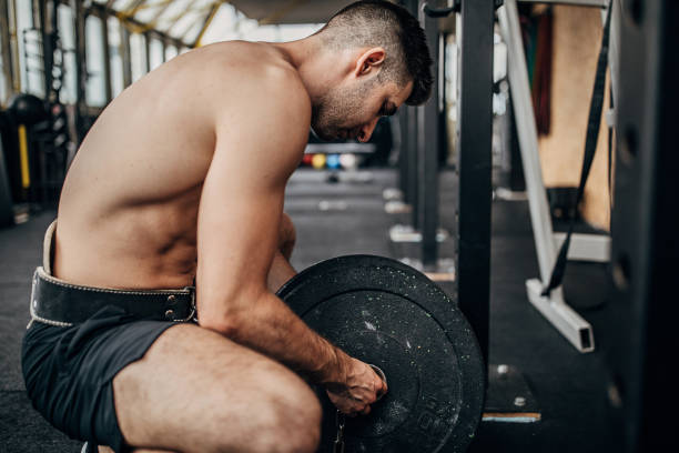 istock Shirtless man preparing weights for training in gym 1253555335