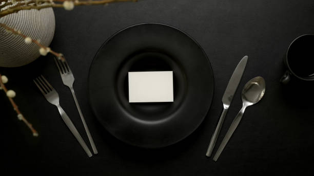 Dark luxury dinning table setting with mock-up place cacd on black ceramic plate, silverware and decoration
