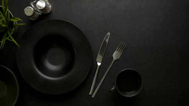 istock Dark luxury dinning table setting with black ceramic plate, silverware, seasoning bottles, copy space and decoration 1253570319