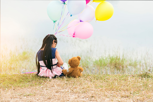 Happy Child hug teddy bear hold air balloon in green park playground. Teddy bear best friend for little kids cute girl. Autism happy playing together holding colorful helium balloons on playground