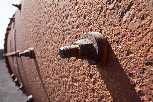 close up of old pitted rusty metal pipe vanishing in the distance with large screws and bolts sticking out