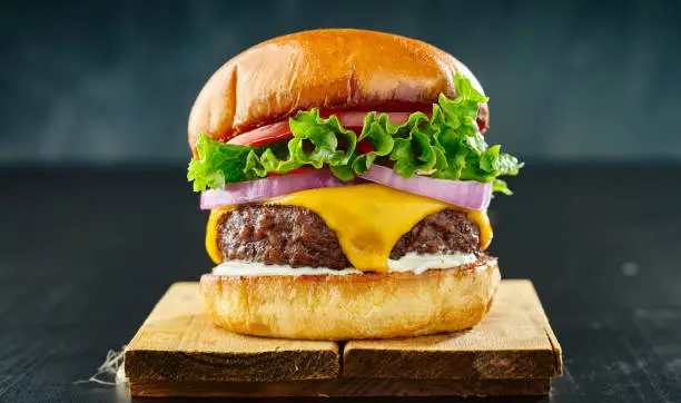 thick cheeseburger with american cheese, lettuce tomato and onion close up