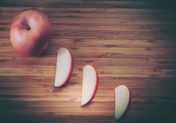 Freshly sliced apple pieces on wooden cutting board in bright kitchen setting.