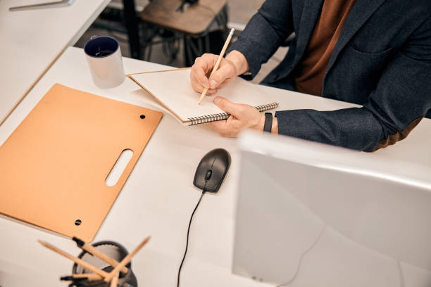 istock Male hand holding pencil with datebook on the white table 1253578936