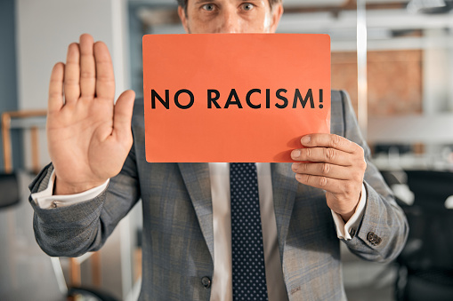 Close up of self confident boss standing at the office and holding a poster with the no racism text in his hand