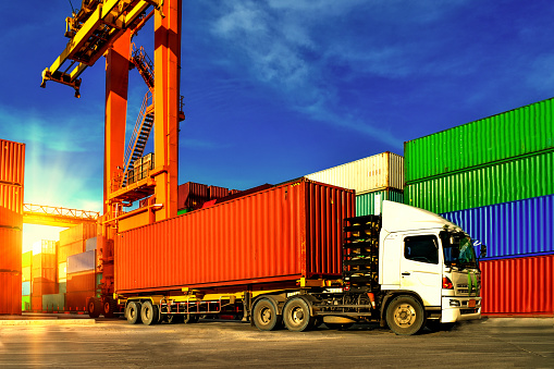 Container handling. Container truck picking up container at yard. Port logistics, container yard operation.Container handling. Container truck picking up container at yard. Port logistics, container yard operation. Container truck or Rubber Tired Gantry Cranes (RTG) picking up a container at yard. Port logistics, container yard operation.