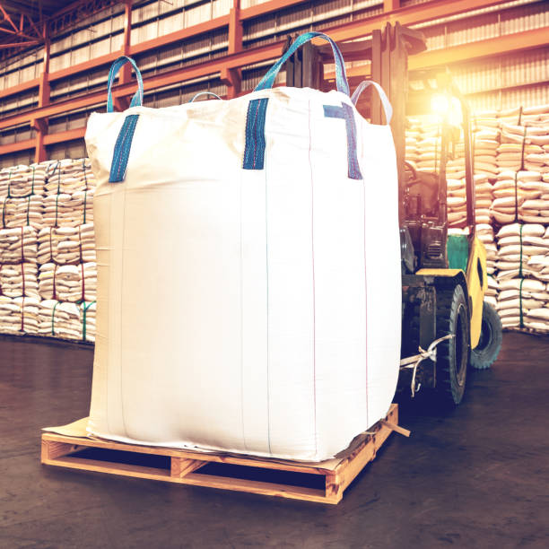 A male worker is driving industrial transporter to hook on large bag and ready to fill one tonne of white rice.