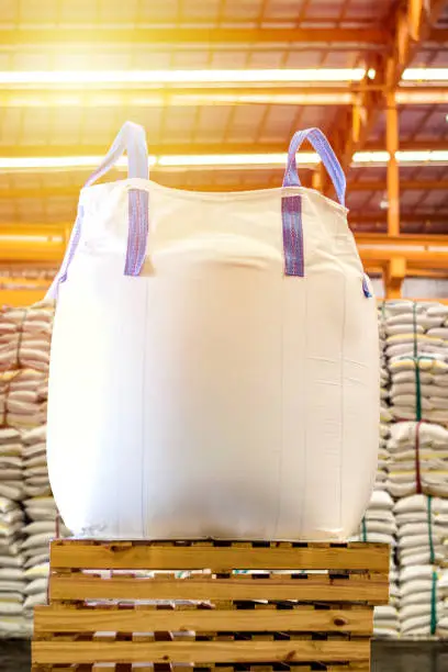 Close up of a jumbo bag on wooden pallet with background of bulk sugar bags.  Sugar bag stuffing container for export.