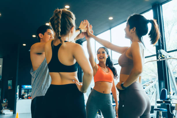 sonríe hombre y mujeres haciendo manos juntas en el gimnasio. grupo de jóvenes haciendo cinco gestos altos en el gimnasio después del entrenamiento. feliz clase de entrenamiento exitoso después del entrenamiento. concepto de trabajo en equipo. - exercising gym health club women fotografías e imágenes de stock