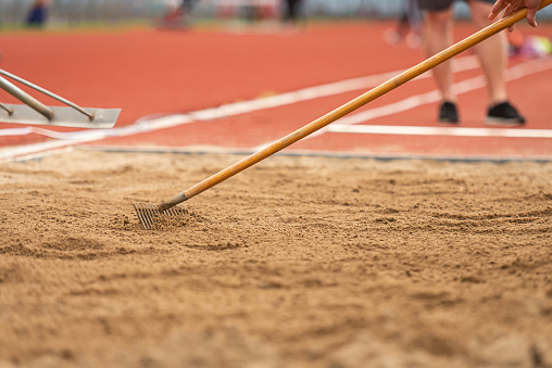 A volunteer raking the sand pit before the next jump in an athletic competition