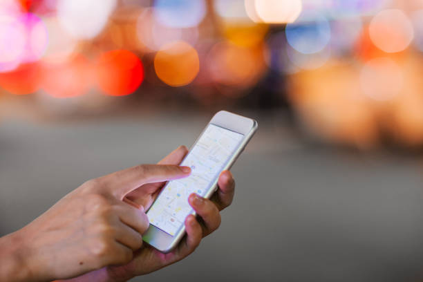 istock Close up view of hands holding mobile phone with map application at night 1253600056
