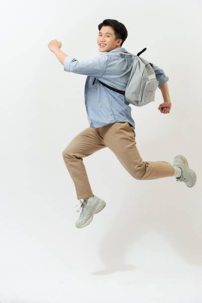 istock happy smiling young man with backpack jumping in air over white background 1253601169