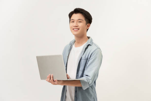 istock Always ready to help. Confident young asian man holding laptop and smiling while standing against white background 1253601287