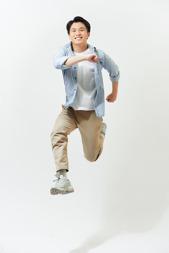 Man dressed in street style clothing is coming downwards after jumping high in the air against blue background