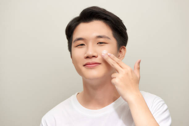 istock Handsome man applying eyes cream close up portrait studio on white background 1253601616