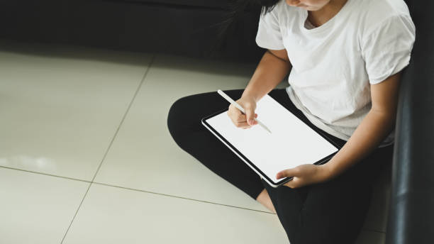 a schoolgirl is using a white blank screen computer tablet and stylus pen at the sitting room. - child office chaos computer monitor imagens e fotografias de stock