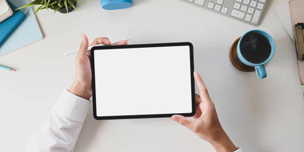 bürotischhände halten ein weißes computertablett mit leerem bildschirm am weißen schreibtisch. - tablet stock-fotos und bilder