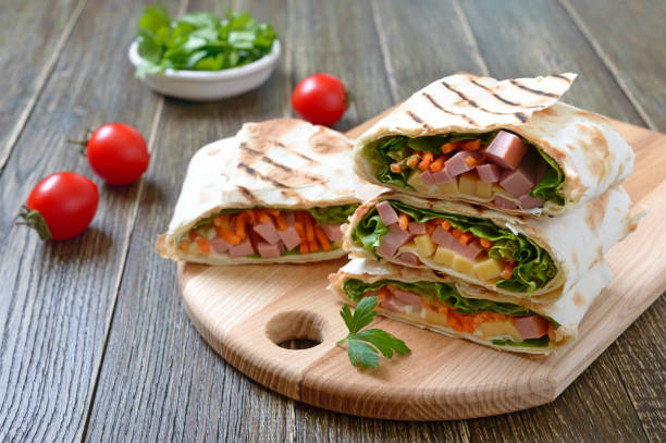 istock Lavash rolls with vegetables, ham and cheese. Tasty breakfast appetizer on a wooden board. 1253608989