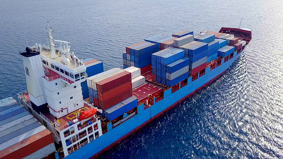 ULCV container ship sails on open water fully loaded with containers and cargo. Large container ship at sea, loaded with various container brands.