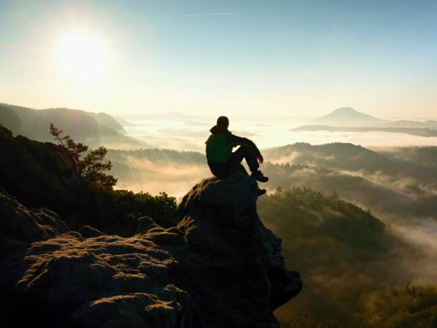 istock Man Tourist Sit On Exposed Rock. View Point With Heather And Branches Above Misty Valley. 1253609347