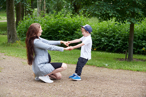 Pregnant woman and her 4 year old son walk in the park. Summer and green trees