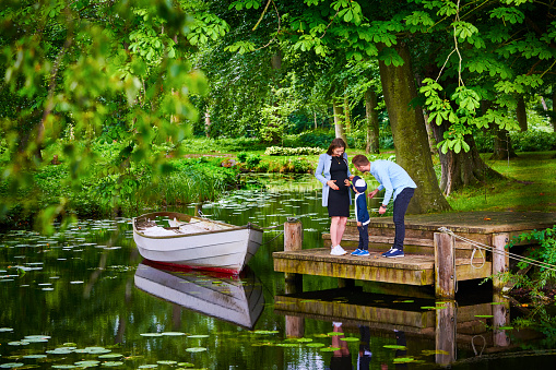 Family standing on small jetty in public park. Boat is tied up to the jetty.