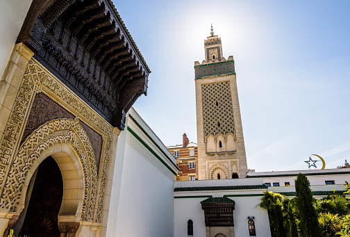 Low angle view of the minaret of the Great Mosque of Paris, seen in backlight from the paradise garden with an imposing sculpted doorway on the left and the star and crescent on the right.