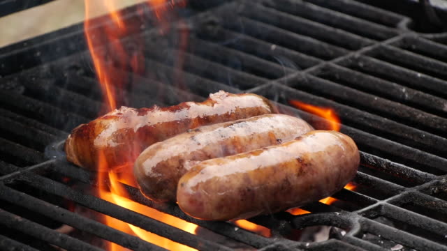Slow motion close-up sausages being cooked on grill