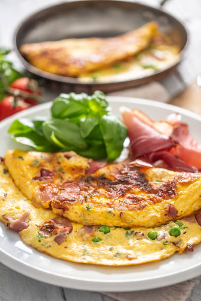 istock Omelette with prosciutto peas basil tomatoes and herbs on white plate. 1253617932