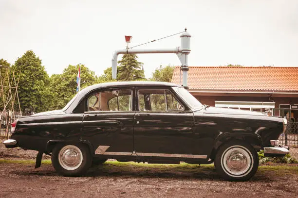 Vintage 1960s Russian executive sedan car parked in front of an old railroad station in the countryside.