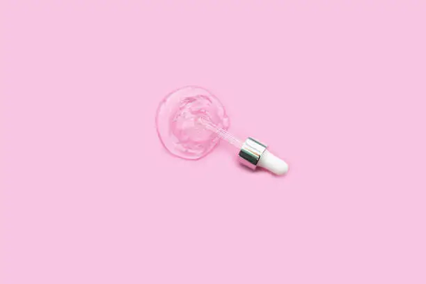 Pipette with dose of lab medicaments or fluid hyaluronic acid on pink background. Cosmetics concept.