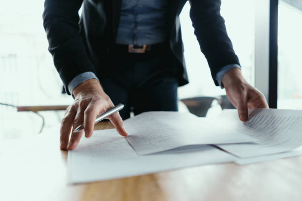 Successful business man signing documents in a modern office Close up hands signing documents in a modern office with window in background. Pen in hand, papers on the wooden desk, futuristic background. legal document stock pictures, royalty-free photos & images
