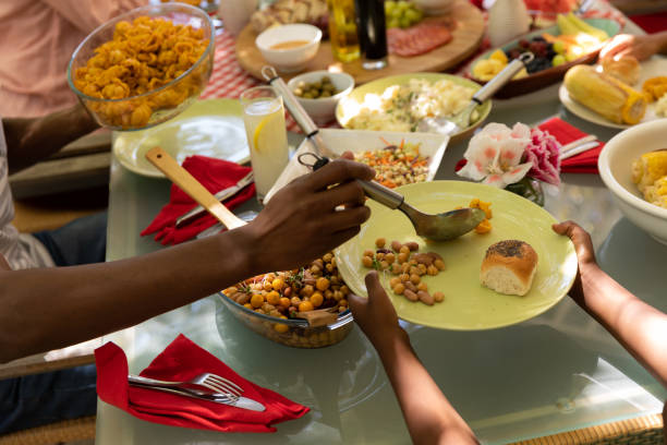 A multi-ethnic, multi-generation family serving food and sitting at a table for a meal outside on a patio, the African American father serving his young son some food while the son holds out his plate