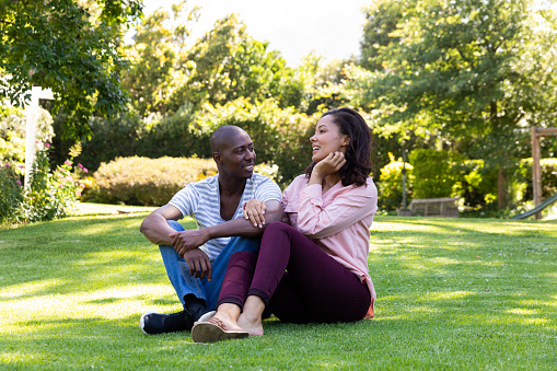 Front view of a mixed race couple outside in the garden, sitting on the grass, talking and smiling