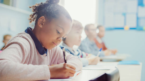 istock In Elementary School Classroom Black Girl Writes in Exercise Notebook, Taking Test. Junior Classroom with Diverse Group of Bright Children Working Diligently, Learning. Low Angle Side View Portrait 1253625295