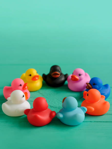 istock Group of multi-colored rubber ducks sit together in a circle on an old wooden turquoise coloured table. 1253626151