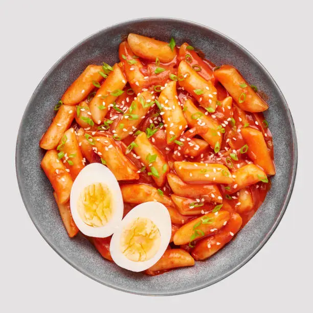 Tteokbokki with eggs in gray bowl isolated on white. Tteok-bokki is a korean cuisine dish of rice cakes and chilli sauce. Asian food. Top view