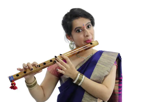Graceful young woman in Indian traditional wear playing a traditional wind instrument called as "Bansuri".