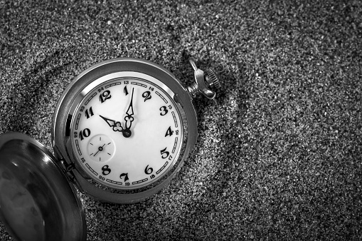 An old pocket watch lying in the sand. The clock fell in the sand. Time is running. Running time. Leaking time.