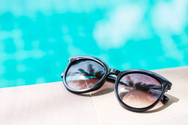 istock Black sunglasses on swimming pool edge with space on blurred blue water background 1253643027