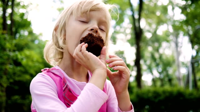 Birthday party. Little girl eating a chocolate cake in the summer park. 4K