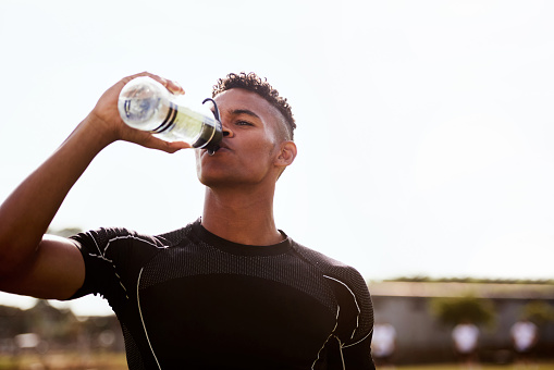 Shot of a young man drinking water after playing a game of rugby
