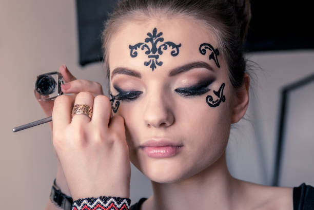 istock Make-up Artist Making a Decorative Black Tattoo on Female Model's Face 1253656492