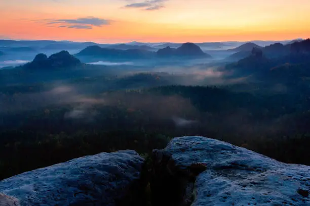 Photo of Kleiner Winterberg before sunrise, beautiful morning view over sandstone cliff into deep misty valley in Saxony Switzerland, foggy background, orange sky, dark night landscape Germany