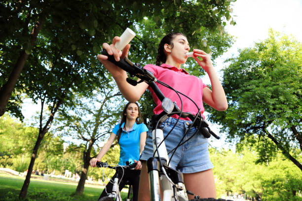 Girl having asthma using asthma inhaler while riding a bike with her sister