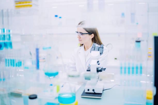 istock Female scientist during research. Using microscope in futuristic lab. Looking through glassware 1253668412