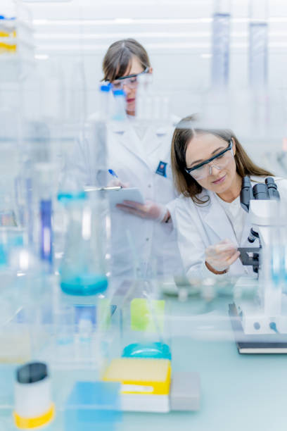 istock Female scientist during research. Using microscope in futuristic lab. Looking through glassware 1253668500