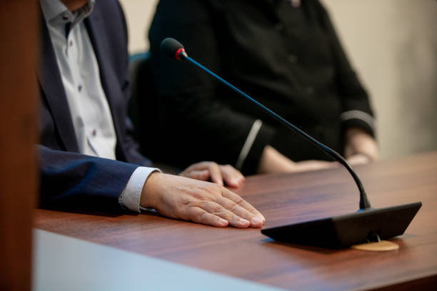 istock A man in a suit speaks while sitting at a table during a business conference or negotiations with business partners. Included microphone and report. Work time. Business style. Shallow depth of field. 1253669676