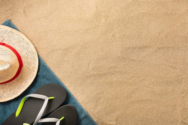 istock Beautiful summer holiday beach background with straw hat and flip flops on sand background, border design, top view with copy space 1253671674